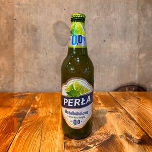 Non-alcoholic Perla beer bottle with lime wedge label on a wooden table surface.