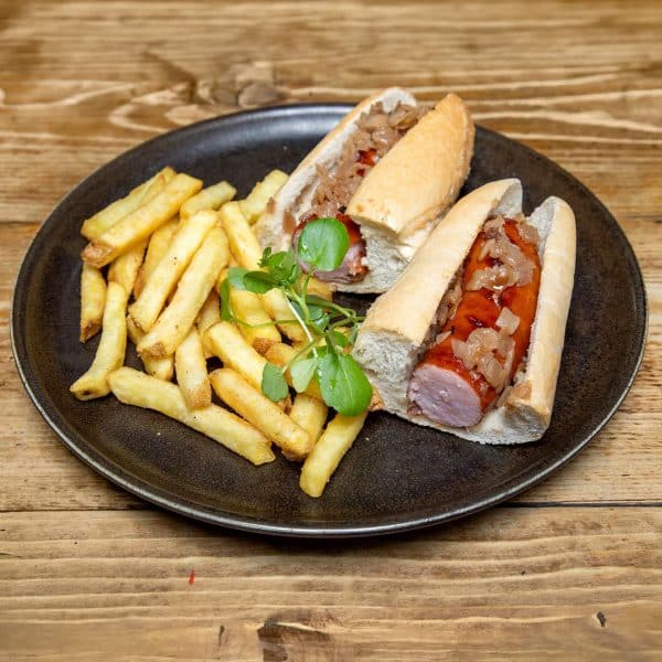 Two hot dogs split lengthwise with onions and sauce, served with French fries on a dark plate.