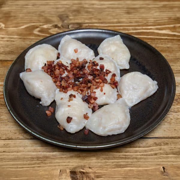 Plate of pierogi topped with crispy bacon bits on a dark plate, set on a wooden table