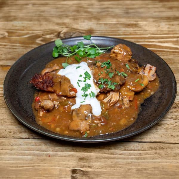 Plate of chicken and vegetable stew in brown gravy, topped with sour cream and chopped parsley on a rustic wooden table.
