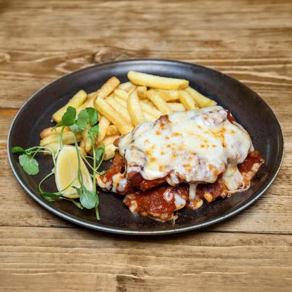 Plate of chicken parmesan with melted cheese and tomato sauce, served with fries, lemon wedge and greens on a dark plate.