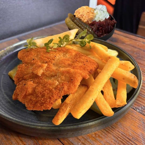 Crispy fried chicken thigh on a bed of thick fries with a small side of pickles and shredded vegetables in a bowl.fter garnish of greens on top of the chicken.