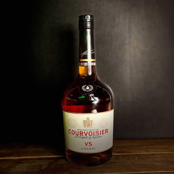 Bottle of CourvoisieR VS cognac on a wooden table against a dark backdrop, with a white label showing the brand name and VS designation