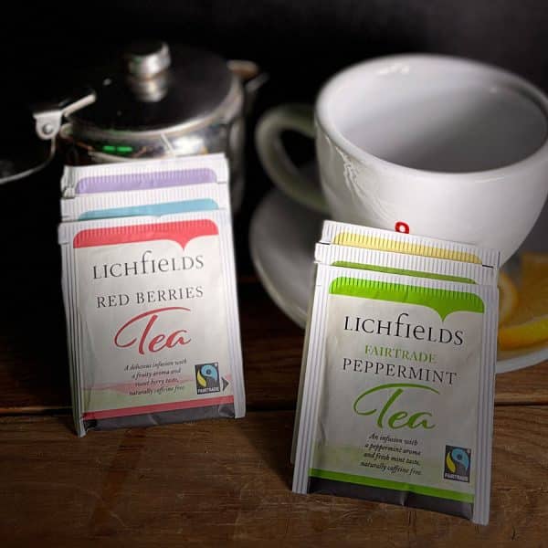 Two boxes of Lichfields tea (Red Berries and Peppermint) stand on a wooden table with a cup and lemon slice in the background.