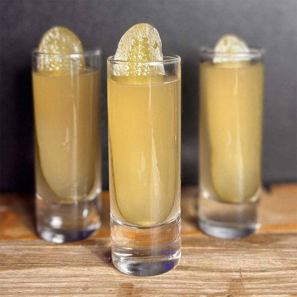 Three tall glasses of pale gold cocktails with a gold leaf garnish, arranged on a wooden bar.